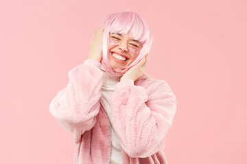 Young laughing happy girl with fur coat and pink hair, touching her head and dancing to music with...