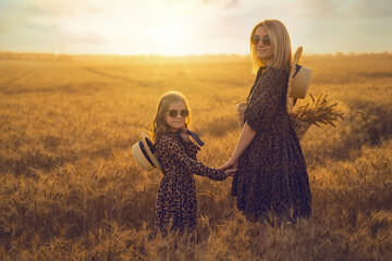 Fashion photo of a young mother and her daughter in leopard print dress and staw hat, same sunglasses at the wheat field on a sunny day © ZaStock