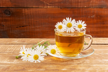Obraz na płótnie Canvas Chamomile medicinal drink in a glass cup on a wooden background. Near daisy flowers.