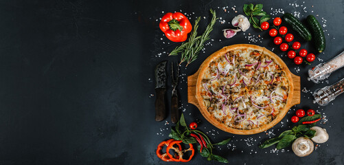 Pizza on the table surrounded by vegetables, herbs and spices.Space for text