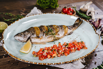Baked fish on a plate surrounded by vegetables, herbs and spices.
