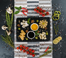Cheese platter with honey, grapes, nuts surrounded by vegetables, herbs, spices