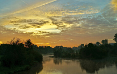 fog on a river with bushes and trees and a colorful sky in the first morning light