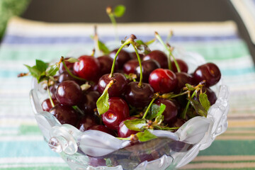 Shaped vase with ripe cherries in water drops with leaves on a striped napkin.