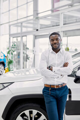 young africanamerican man came to see automobiles in dealership or cars showroom, he stands next to...