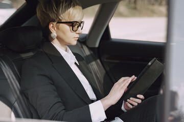 Businesswomanin a car. Lady in a black suit. Woman use a tablet.