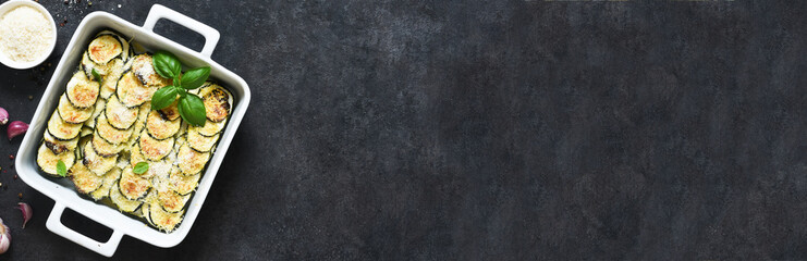 Zucchini casserole with cream, garlic and parmesan on a black background. View from above.