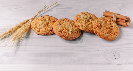 composition of baked oatmeal cookies decorated with cinnamon sticks and wheat, oat flakes on  white wooden table background. copy space. image design for menu layout