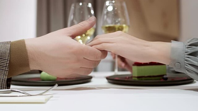 Close up of hand of unrecognizable man taking hand of his unrecognizable girlfriend. Unrecognizable couple sitting in cafe and drinking champagne