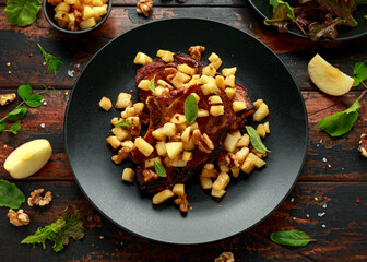 Roasted Pork chops with caramelized apples, walnuts and sage in black plate on wooden table