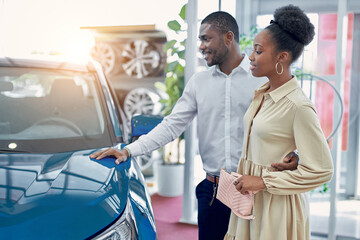 Obraz premium confident handsome afro man shows to wife a car he is liked, they look at car and discuss, man and woman think before making purchase