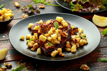 Roasted Pork chops with caramelized apples, walnuts and sage in black plate on wooden table