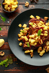 Roasted Pork chops with caramelized apples, walnuts and sage in black plate on wooden table