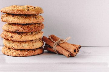 Stack of oatmeal cookies and a bunch of cinnamon sticks on a wooden table on a white background. Image design for menu layout. Tasty and junk food concept.  Front view.