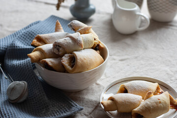 Homemade pastry. The rugelach with jam in a white bowl on a table. Traditional Jewish holiday cookie. Bagels. Croissants. Still life photography with cookies.