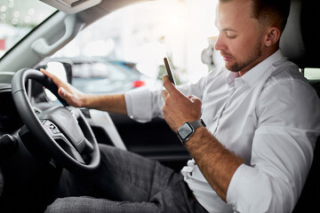 young caucasian handsome business man test drive new car. guy is examining new car's design and interior in car dealership