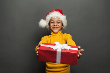 Happy African American child Santa holding red Christmas box with white silky ribbon on black background