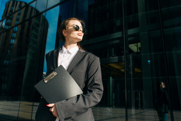 A portrait of young feminist leader businesswoman with clipboard standing outdoors. Copy space.