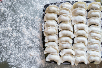 Dumplings - ukrainian traditional vareniki, filled with cherries on a black plate on a glass table.