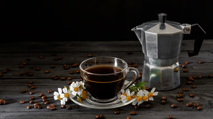 Hot coffee in a coffee cup and roasted coffee beans with flowers beside the cup on a dark tone wood floor and copy space.