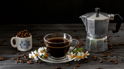 Hot coffee in a coffee cup and roasted coffee beans with flowers beside the cup on a dark tone wood floor and copy space.