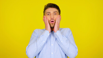 Surprised man in a light blue shirt on a yellow background with copyspace. The bearded guy is shocked by what he saw