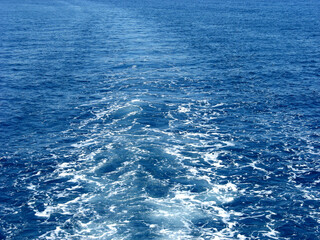 Blue sea waves with white foam. Water behind a ship. Boat wake in the sea, on a brilliant sunny day. This is the view behind a car ferry. Trail print on water surface. Sunny day scenery, blue water 
