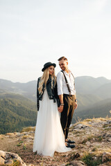 Naklejka premium Amazing smiling wedding couple. Pretty bride and stylish groom. Bride and groom are standing face to face with the green forest and mountaints on background.