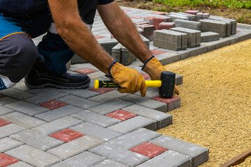 A gloved craftsman lays paving stones in layers. Brick paving slabs for professional use. Laying gray concrete paving slabs in the courtyard of the house on a sandy foundation.