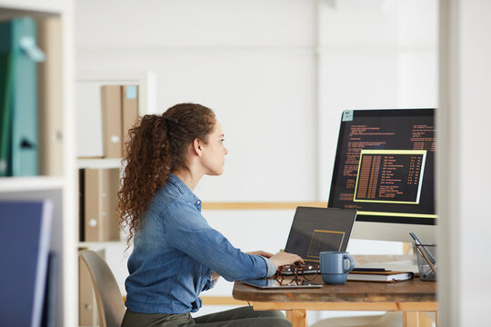 Side view portrait of female IT developer using computer while coding in modern white office interior, copy space