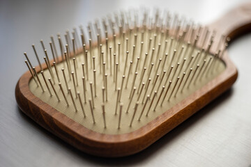 Wooden massage hair brush with iron bristles, macro side view on the shiny grey table.