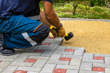 A gloved craftsman lays paving stones in layers. Brick paving slabs for professional use. Laying gray concrete paving slabs in the courtyard of the house on a sandy foundation.