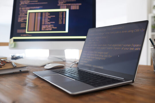 Close up background image of black and orange programming code on computer screen and laptop in contemporary office interior, copy space