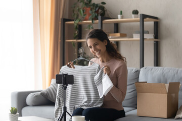 Happy satisfied Caucasian female client blogger shoot clothing unpacking on cellphone camera at...