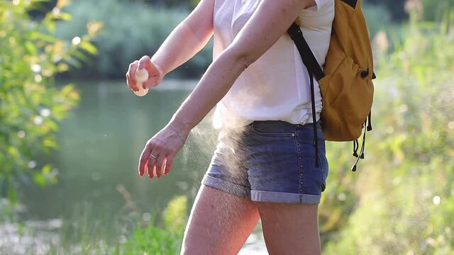 Woman spraying insect repellent against mosquito and tick on her arms and legs during hike in nature. Skin protection against insect bite