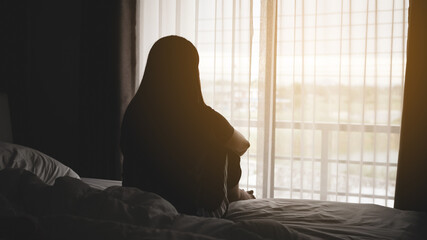 silhouette of alone woman sitting on the bed beside the windows with sunlight in the morning	