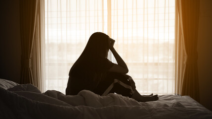 silhouette of alone woman sitting on the bed beside the windows with sunlight in the morning	