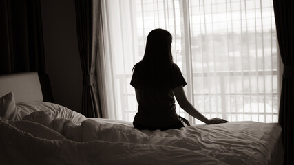 silhouette of alone woman sitting on the bed beside the windows with sunlight in the morning	 - Powered by Adobe