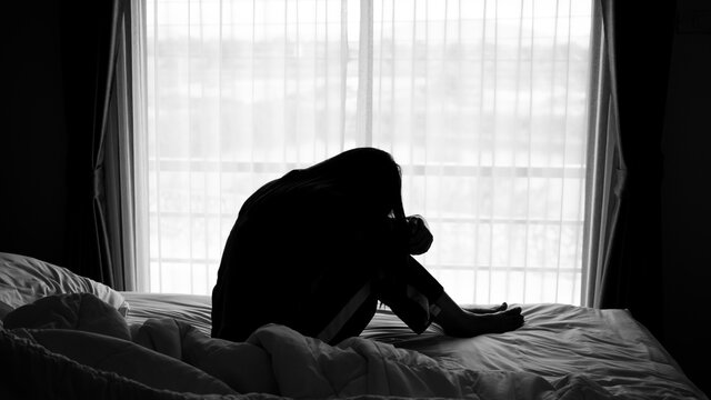 silhouette of alone woman sitting on the bed beside the windows with sunlight in the morning	