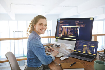 Portrait of female IT developer smiling at camera while typing on keyboard with black and orange...