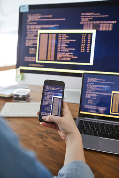 Vertical close up of female hand holding smartphone with code on screen while working at desk in office, female IT developer concept, copy space