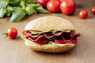 sandwich with beef, tomatoes and salad on a wooden background