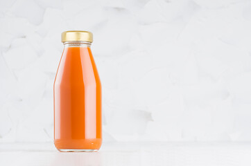 Carrot juice in glass bottle with gold cap  mock up on white wood table in light interior with copy space, template for packaging, advertising, design product, branding.