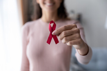 Crop close up focus of woman hold red ribbon show support for patients sick with breast cancer,...
