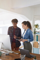 Vertical portrait of female IT developer talking to African-American colleague while standing by computers in modern office, copy space above