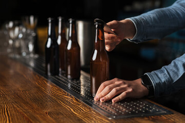 Beer industry. Bartender opens bottle of ale without label on wooden bar counter