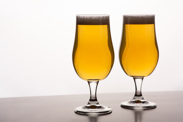 Two glasses of light beer with foam on table and on white background