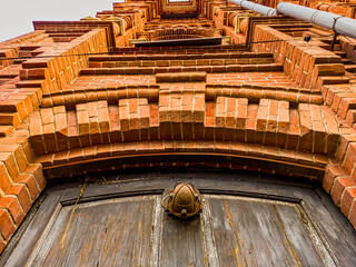 look from below at an old brick building with a fragment of a wooden door in the foreground