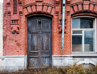 Fototapeta na wymiar The wooden door in the wall of the old brick building is closed and there is a window nearby