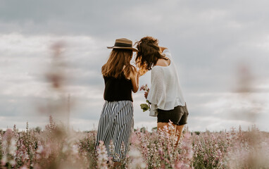 Back side shot of two young women looking at mobile phone, taking photographs in a sage flower field
